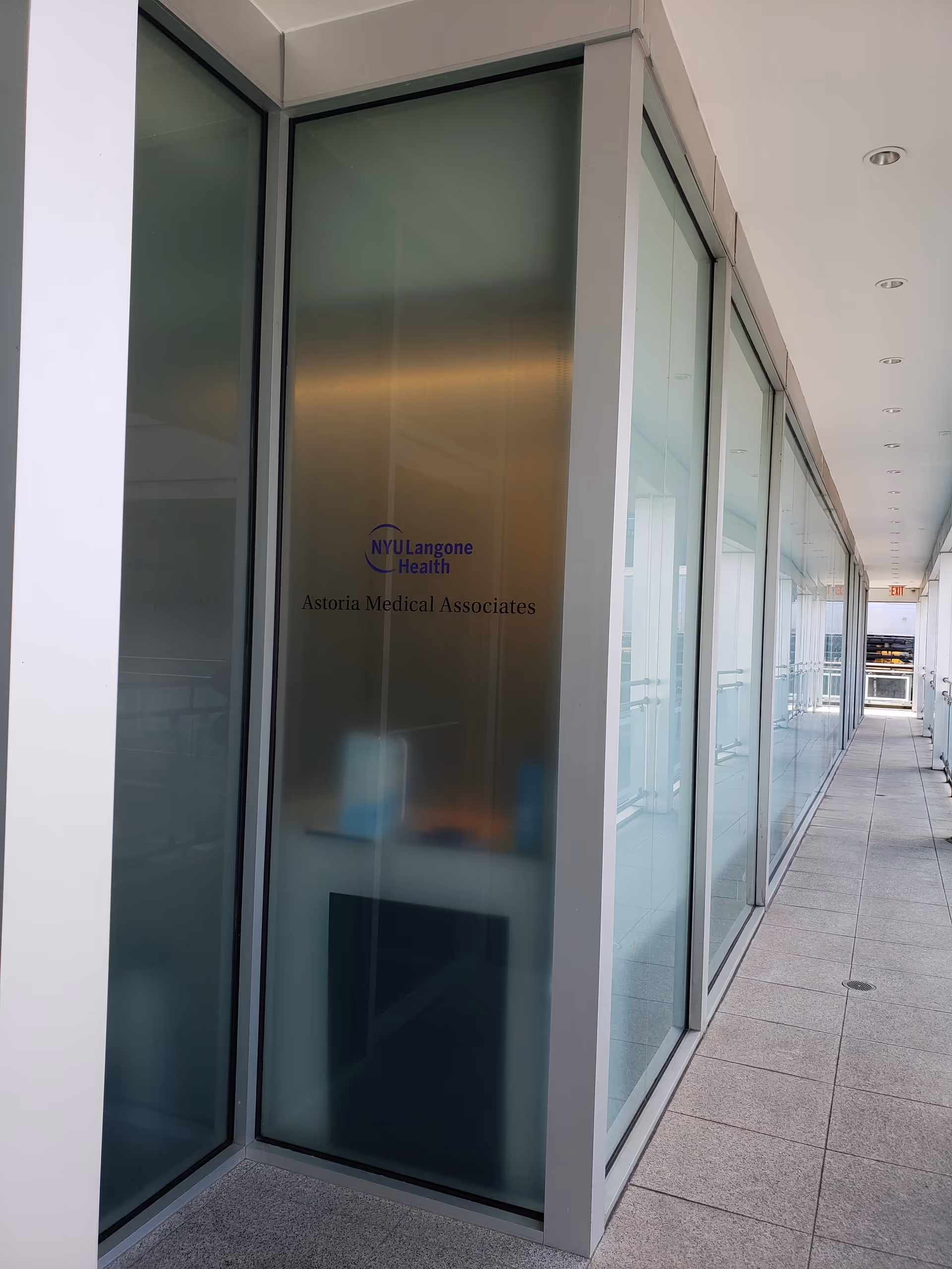 Long glass-walled corridor inside a building displaying NYU Langone Health Astoria Medical Associates.