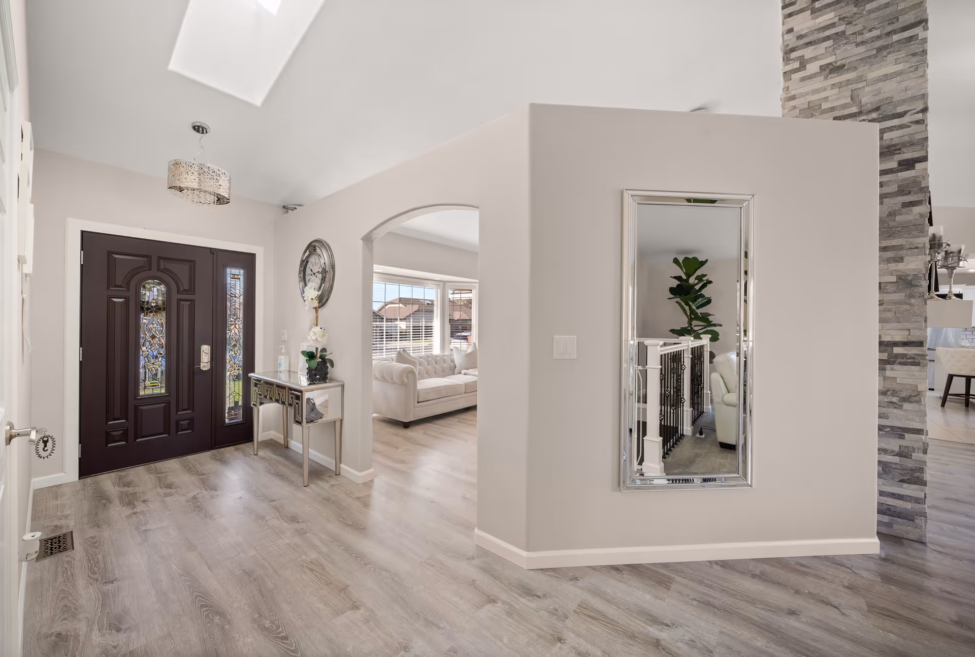 Bright entry foyer with dark front door, console table, mirror, and archway to living area