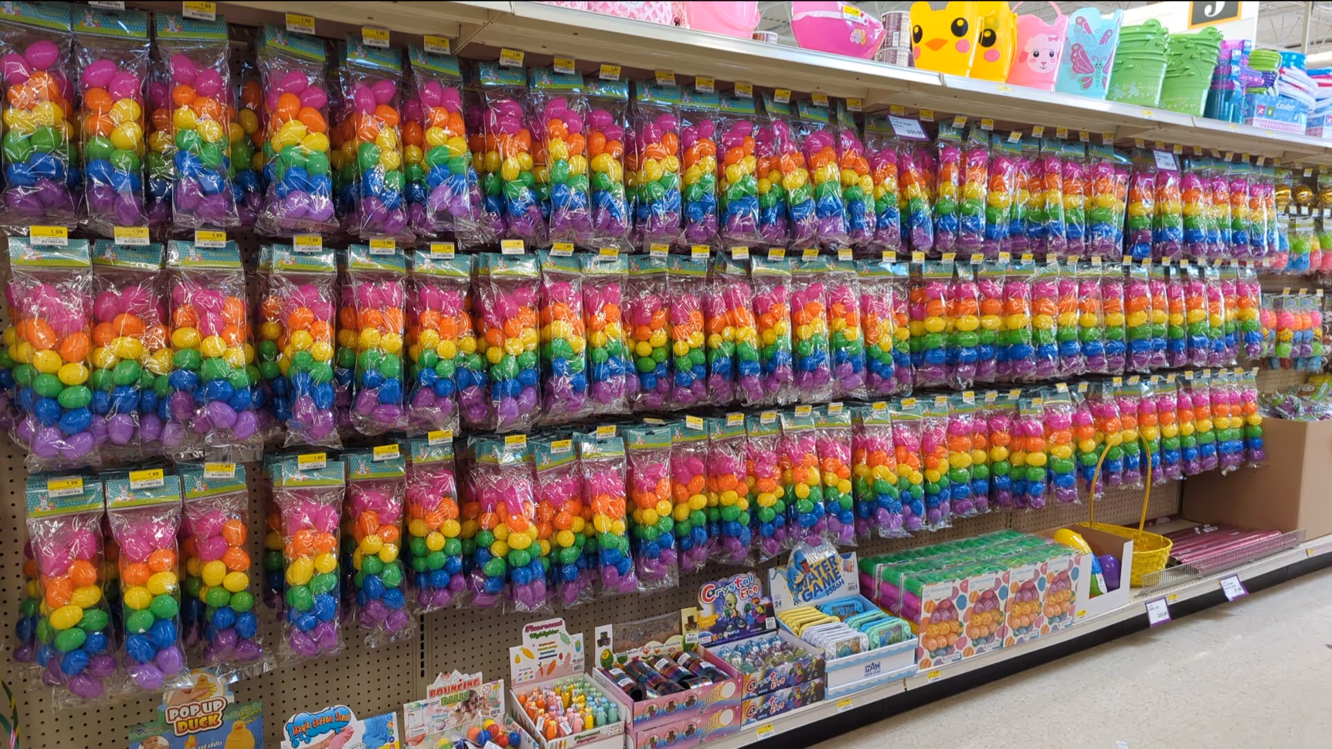 Aisle of rainbow-colored plastic toys in bags on Discount Drug Mart store shelves.