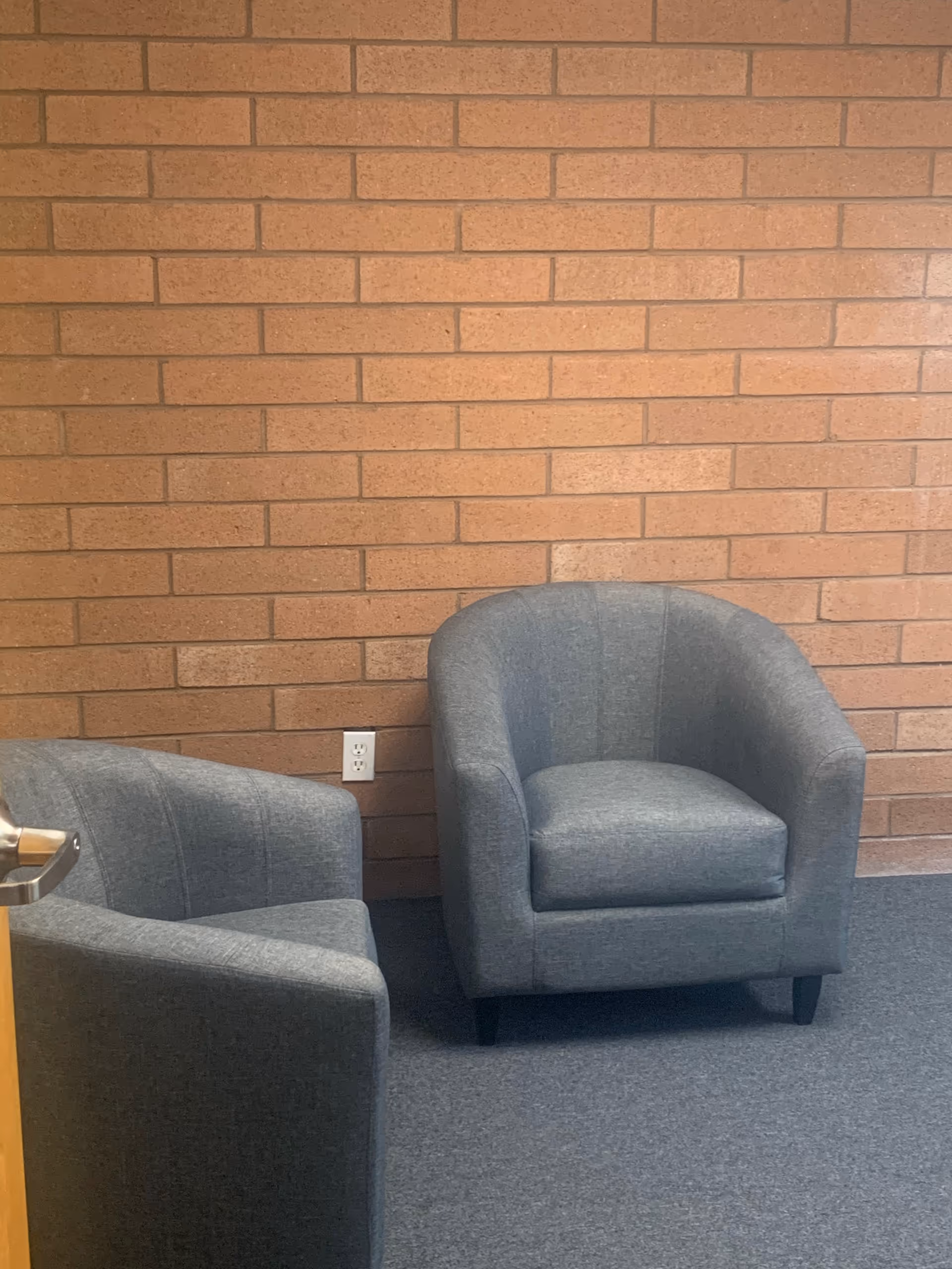 Two gray upholstered armchairs sit against a brick wall in a quiet interior lounge.