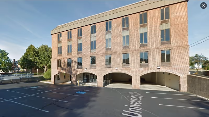 Three-story brick building with arched ground-floor openings and a parking lot in front.