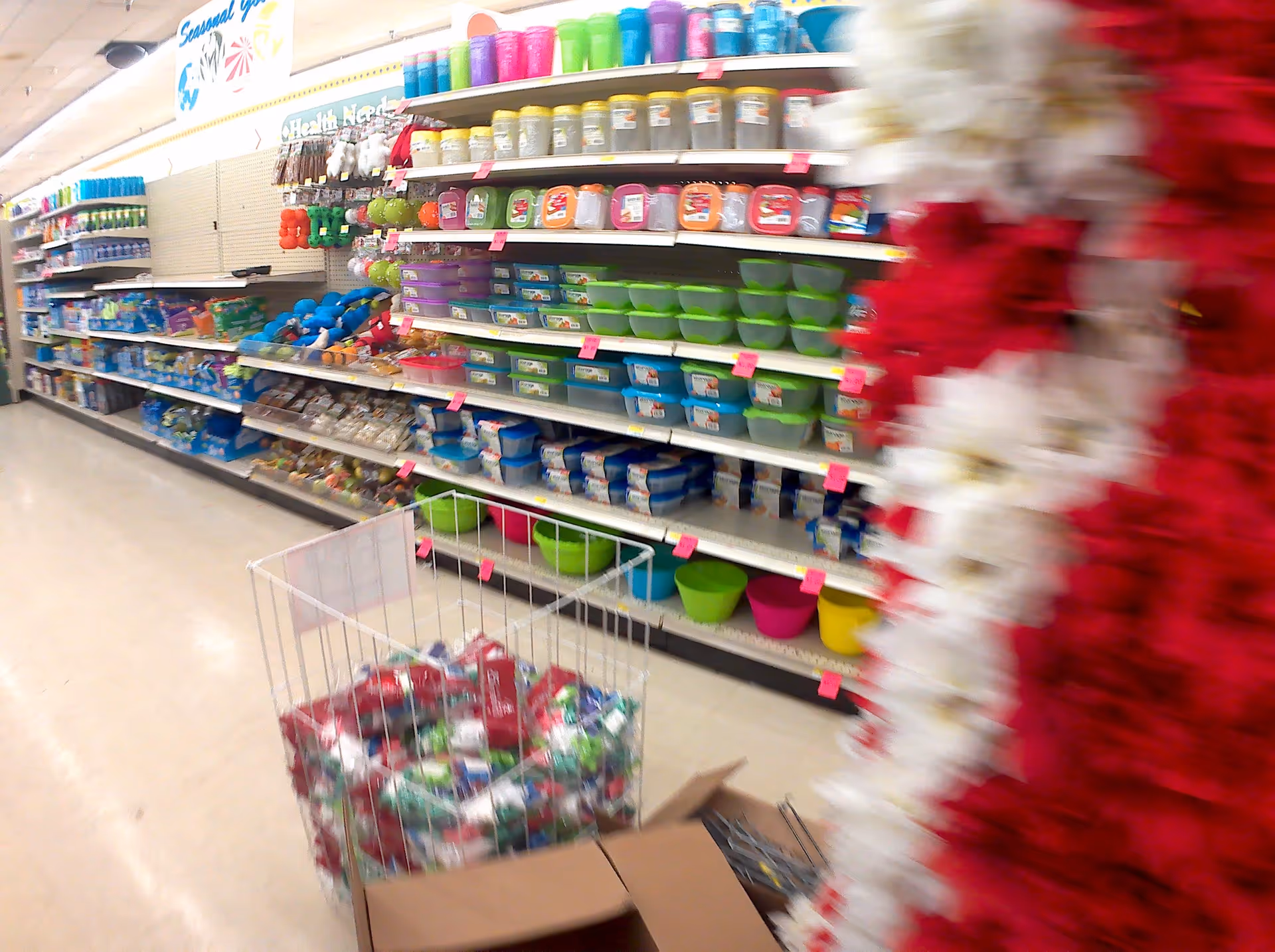 Aisle of a discount store with colorful bowls and a cart in foreground