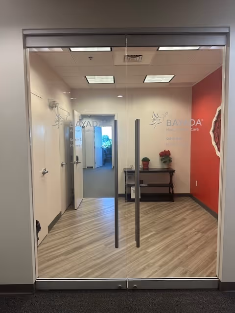 Glass double doors open to a hallway with a table, red wall, and BAYADA logos.