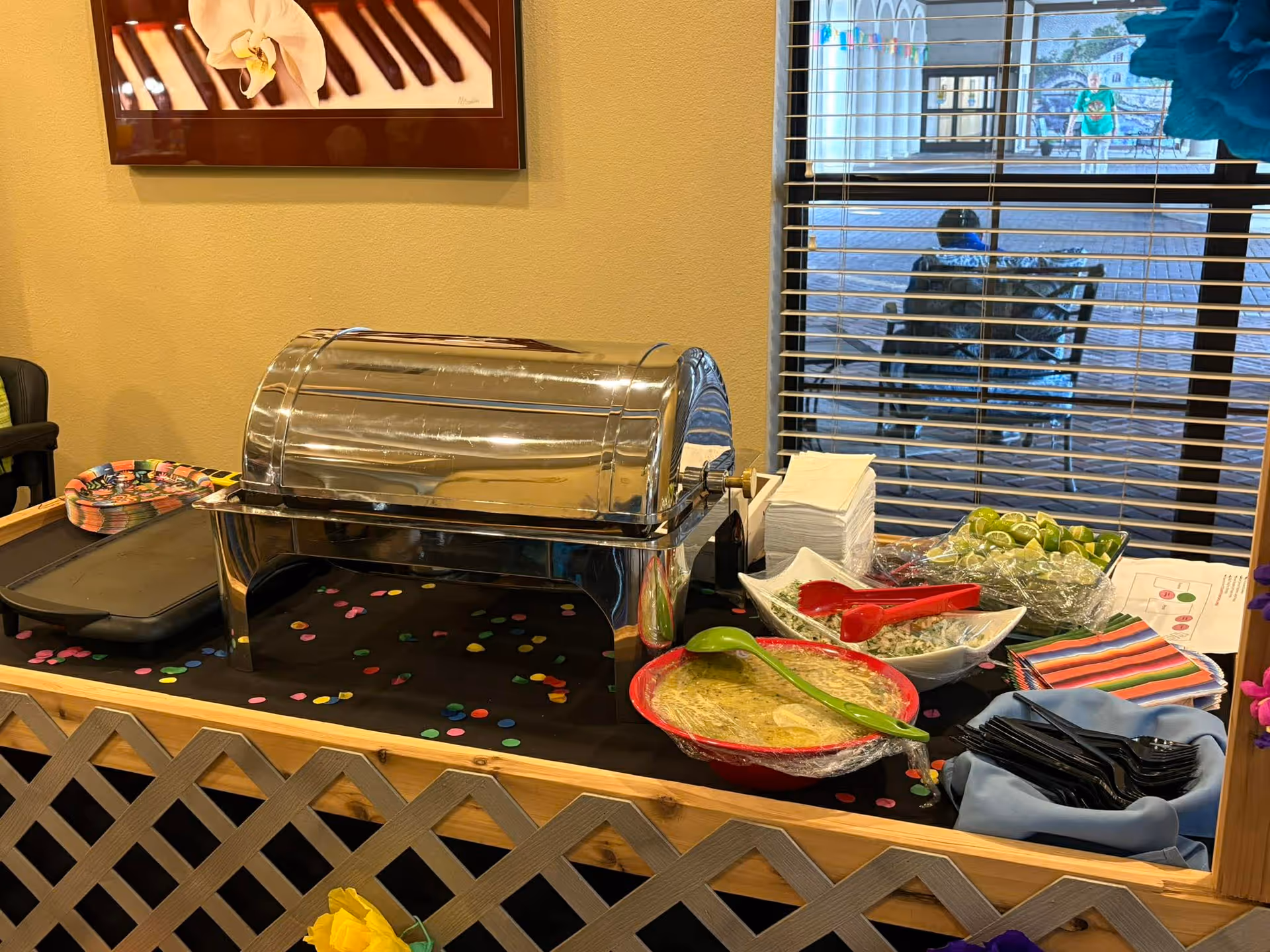 Buffet setup with chafing dish, bowls, plates, and colorful confetti on a dining table.