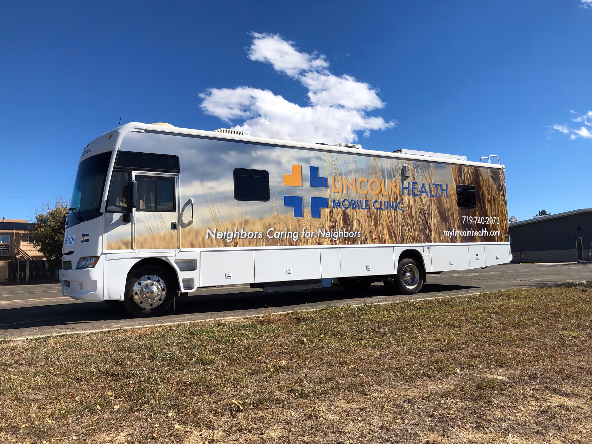 White Lincoln Health Mobile Clinic bus parked outdoors beside a building under blue sky.