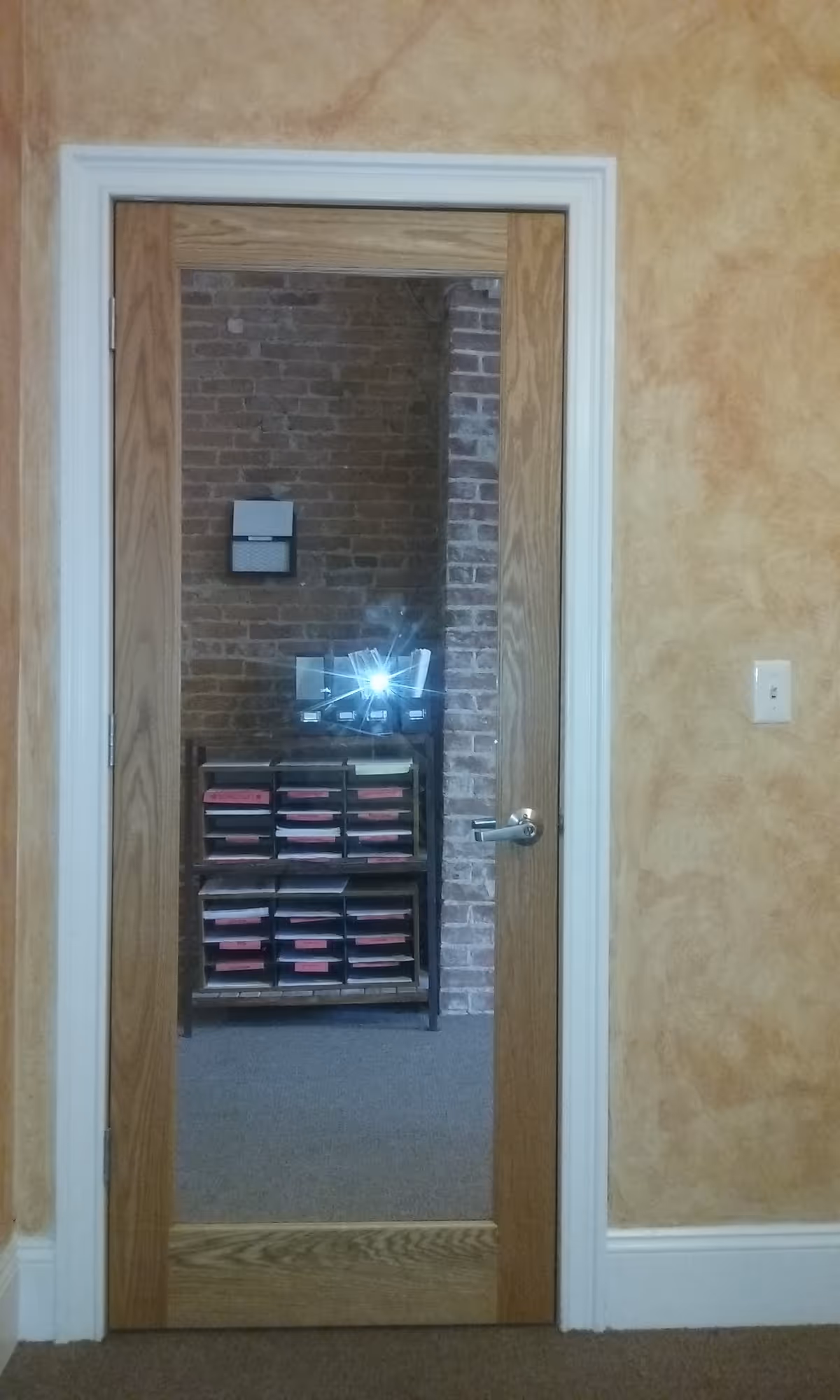 Open wooden door reveals a brick-walled room with shelves and a monitor.