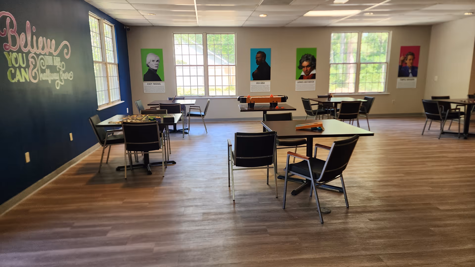 Bright community room with tables, chairs, and wall posters in a senior facility.