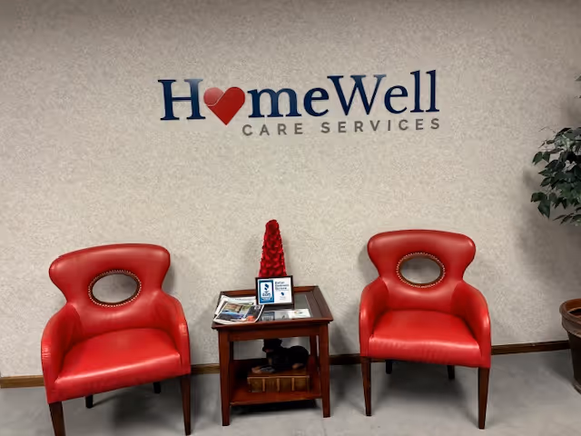 Two red chairs and a small table in a lobby under HomeWell Care Services