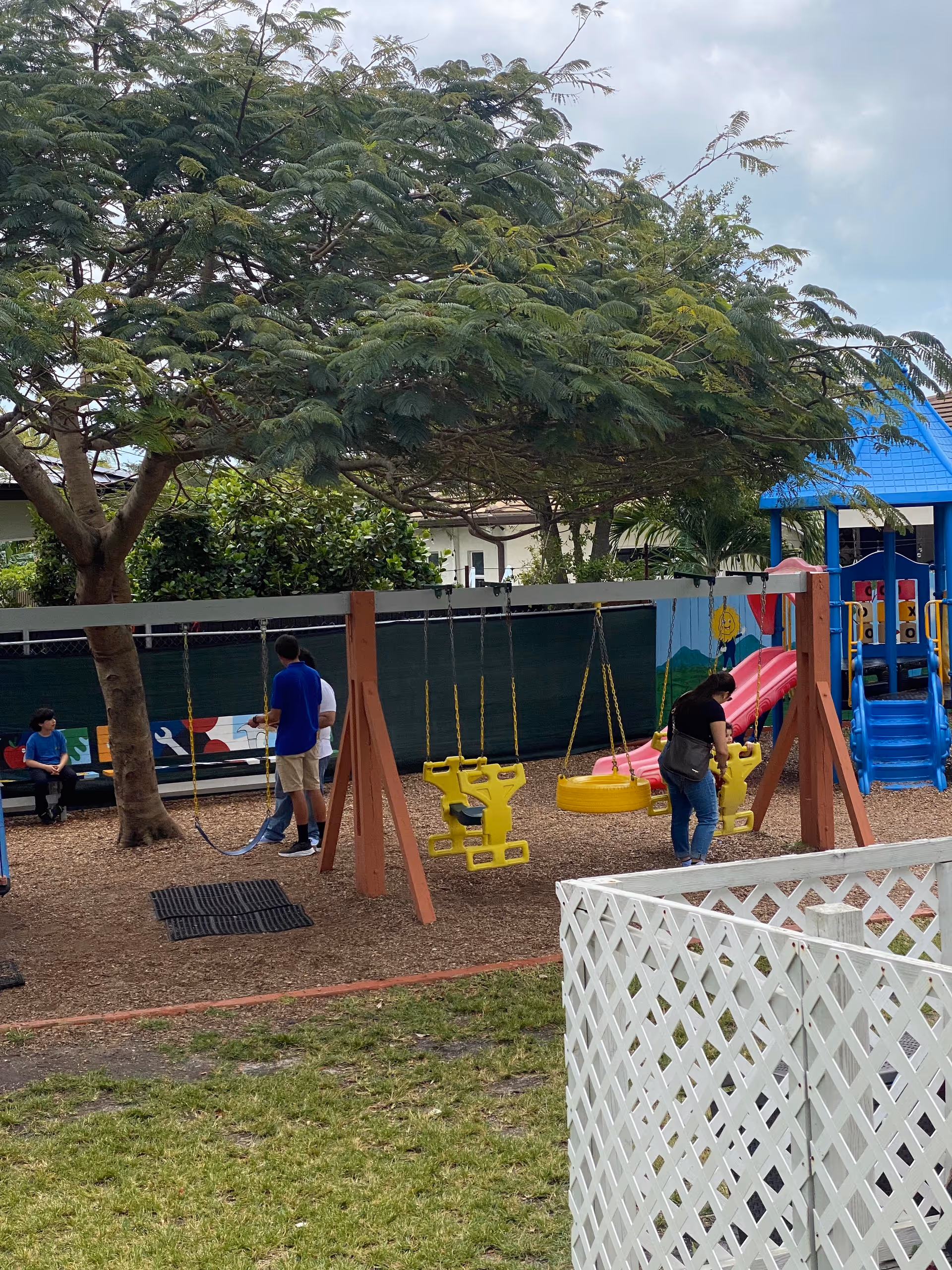 Outdoor playground area with swings, a slide, and people near equipment.
