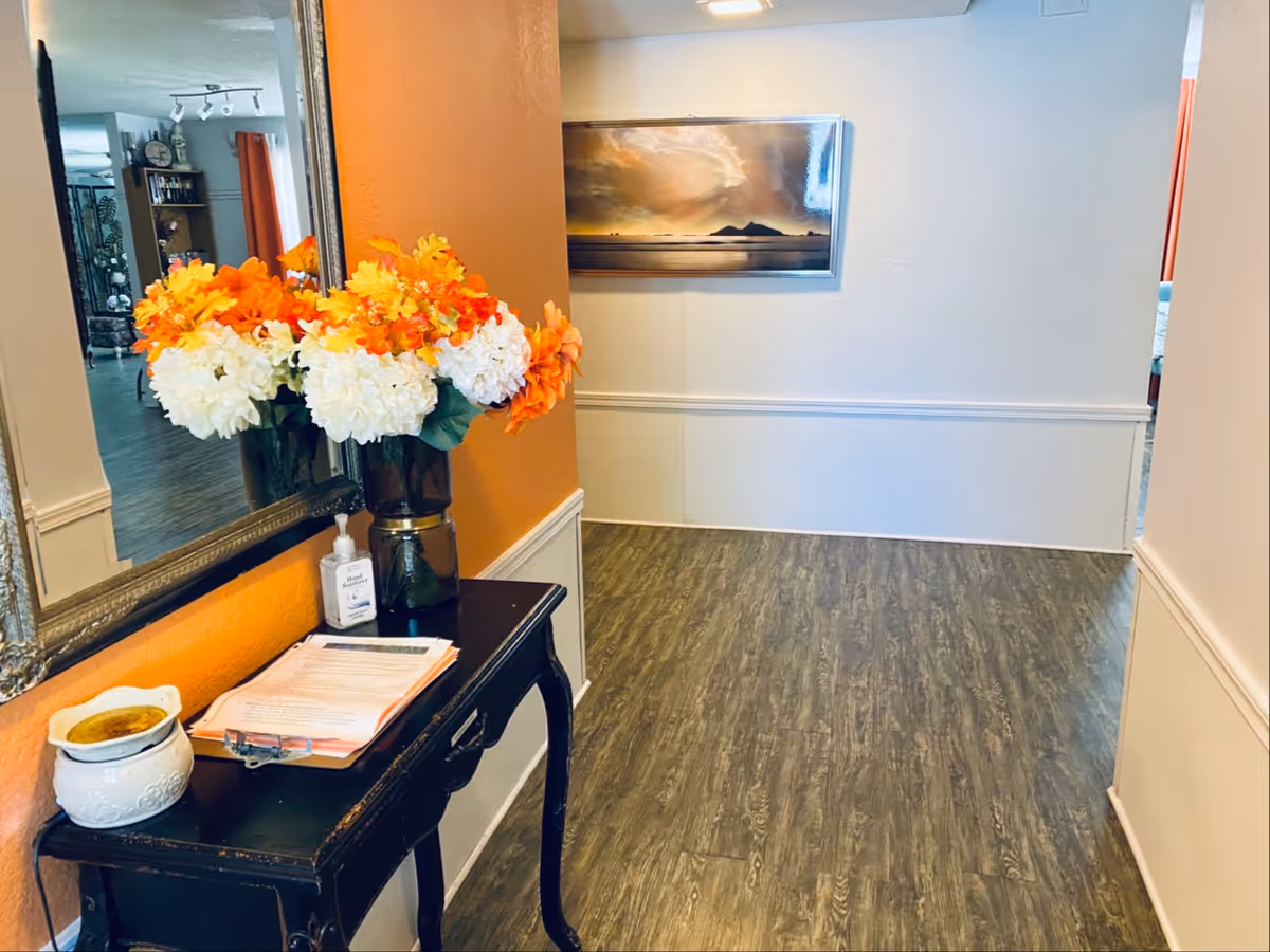 Interior hallway with a console table, orange and white flowers, and framed wall art.