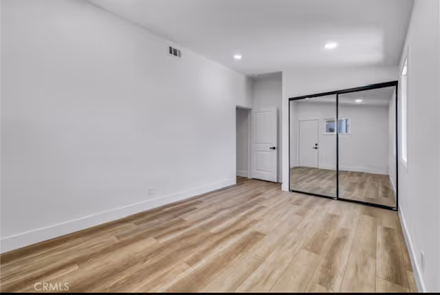 Bright, empty interior room with wood flooring, white walls, and mirrored closet doors.