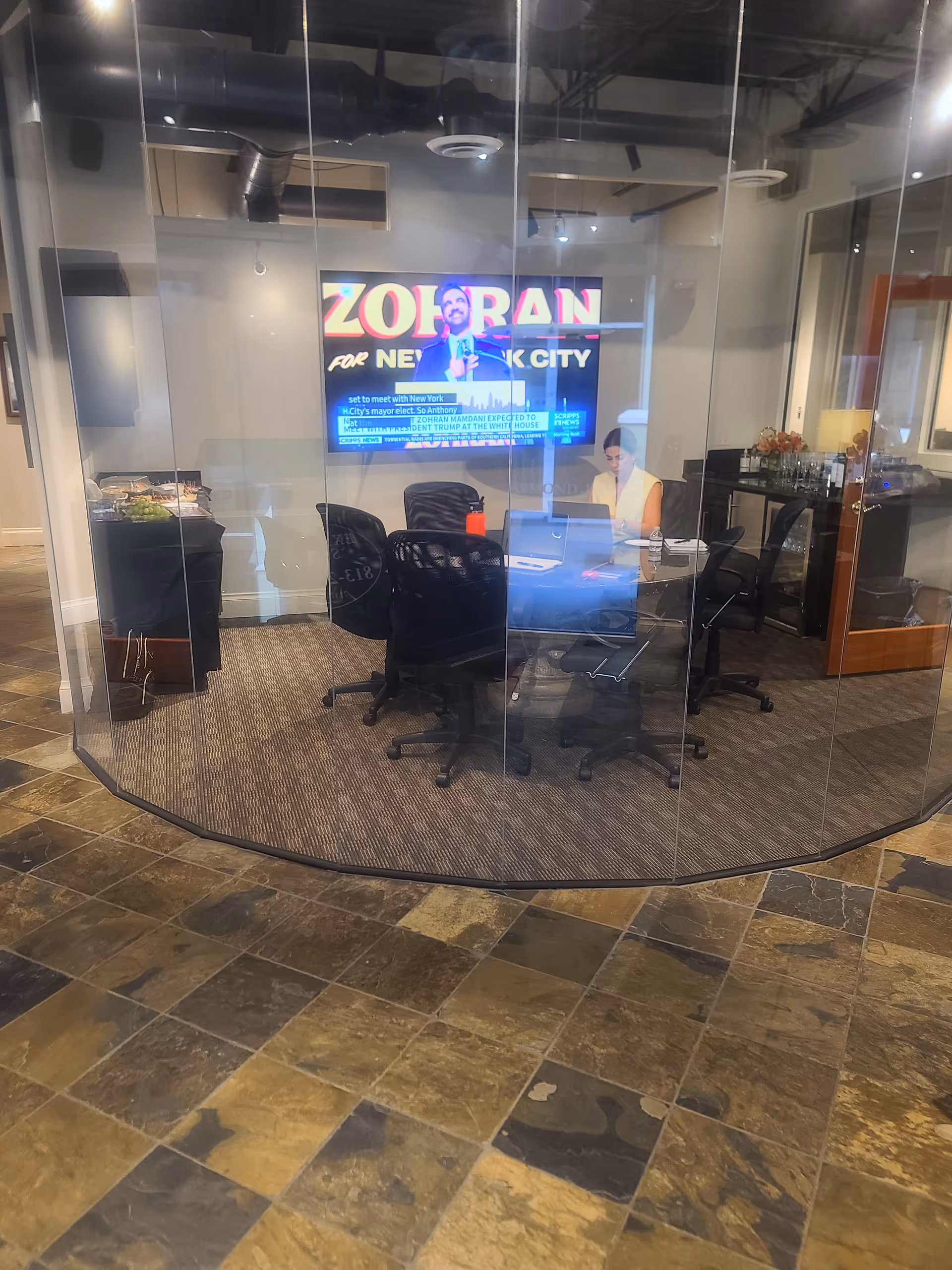 Curved glass-walled conference room with chairs and a staff desk visible.