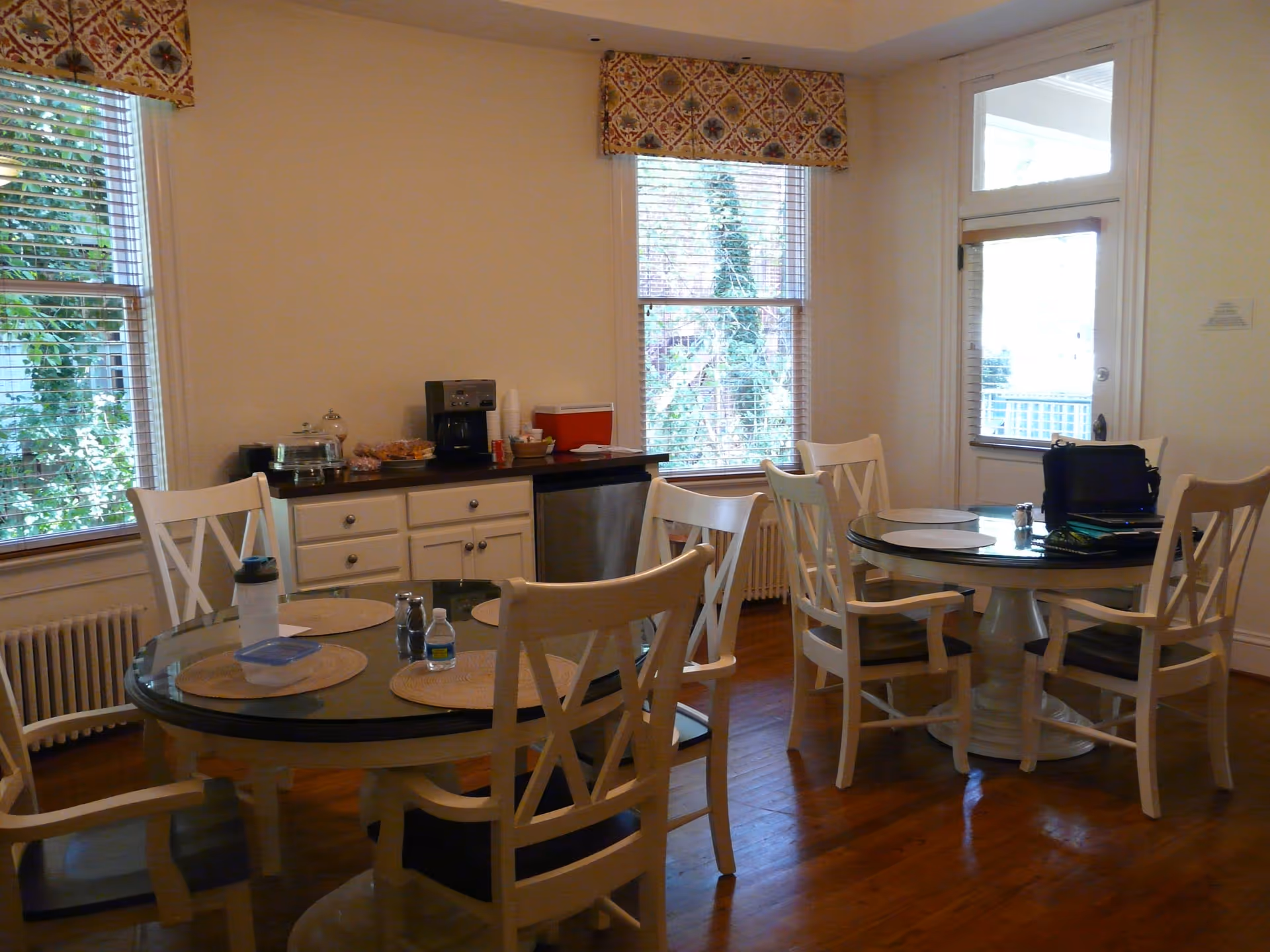 Bright dining room with round tables, white chairs, and a coffee station along cabinets.