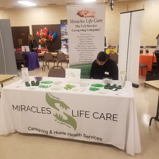 Indoor exhibit table for Miracles Life Care with banners and staff.