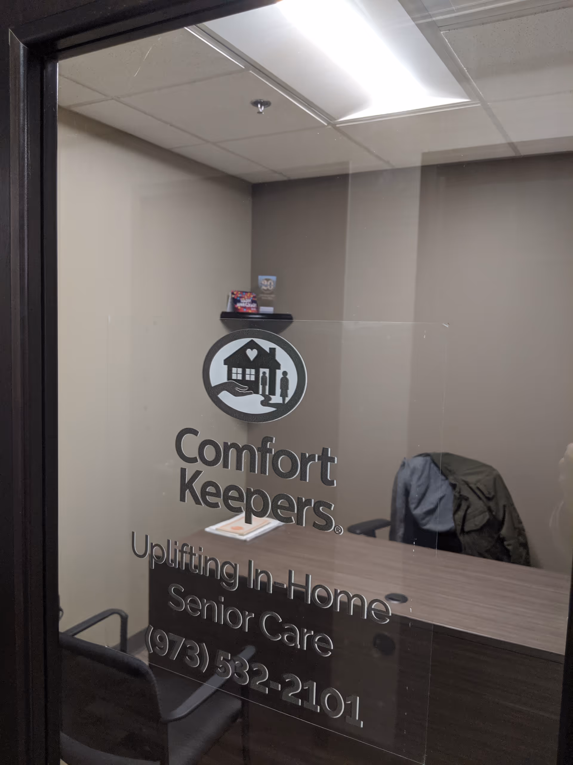 Glass door with Comfort Keepers logo, reception desk, and a coat draped over a chair.