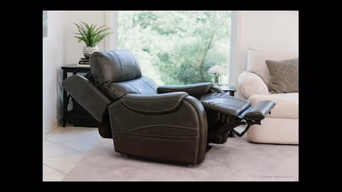 A black leather reclining chair in a bright living room with a beige sofa and greenery