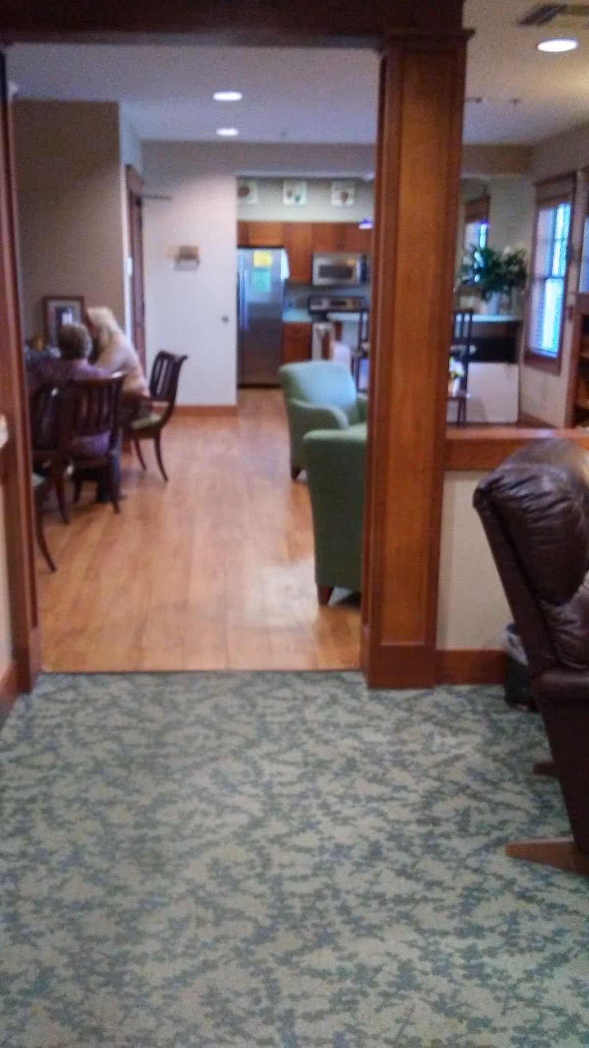 Interior common area of hospice facility with dining tables, chairs, and a kitchen in background.