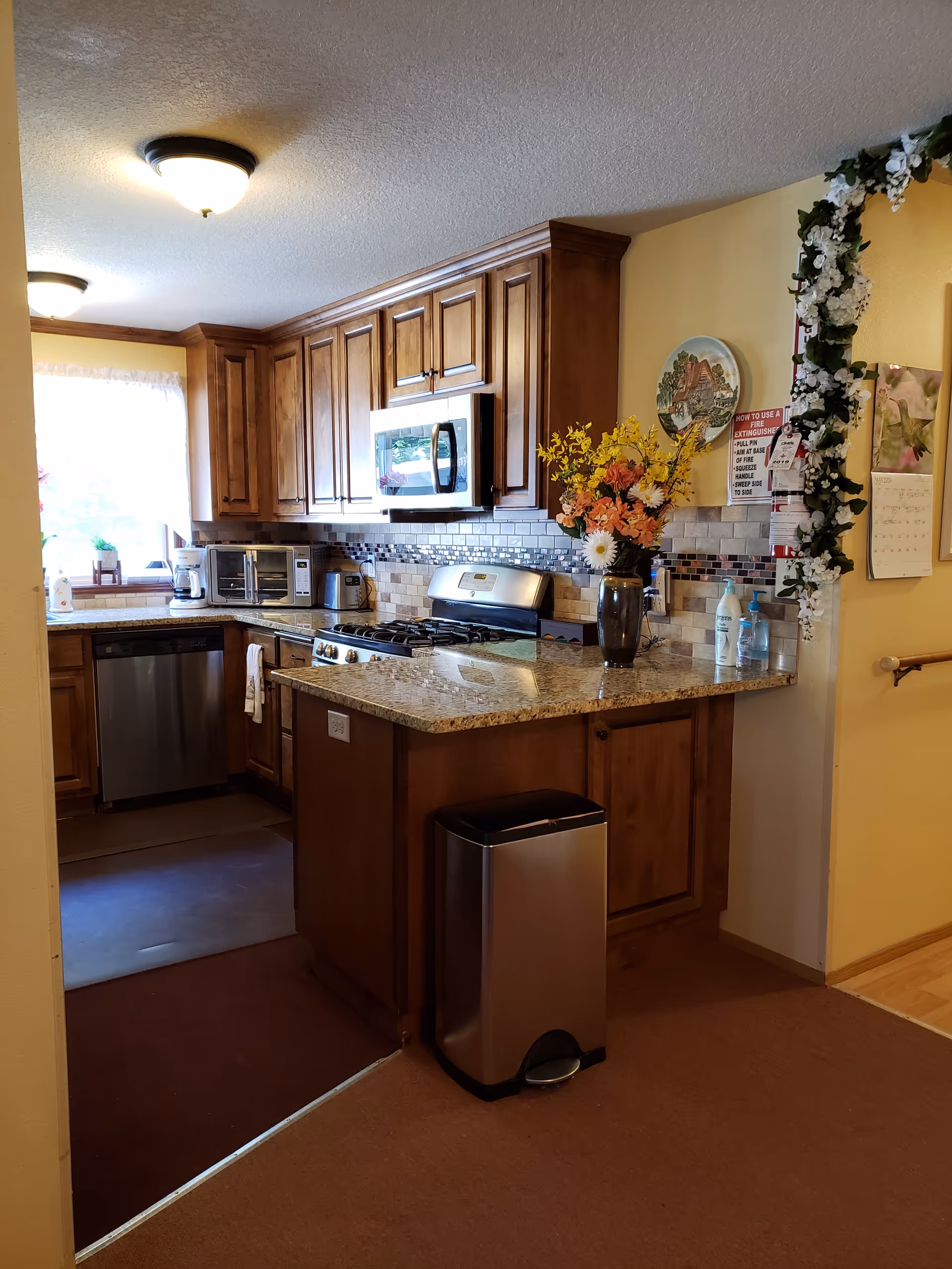 Senior living facility kitchen with wooden cabinets, granite island, and stainless appliances.