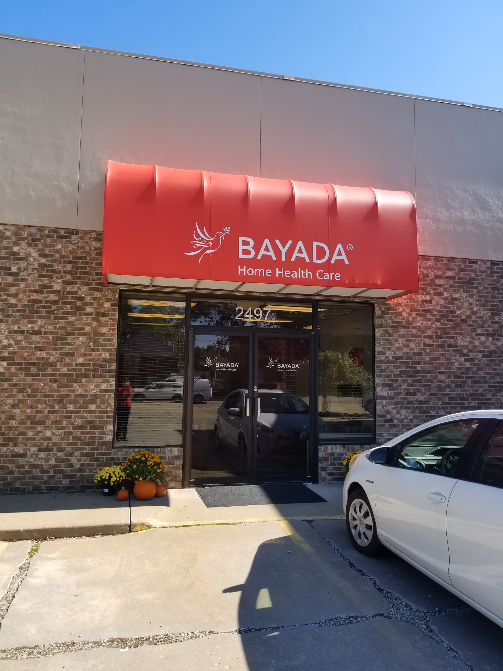 Exterior view of a BAYADA Home Health Care storefront with a red awning and glass doors.