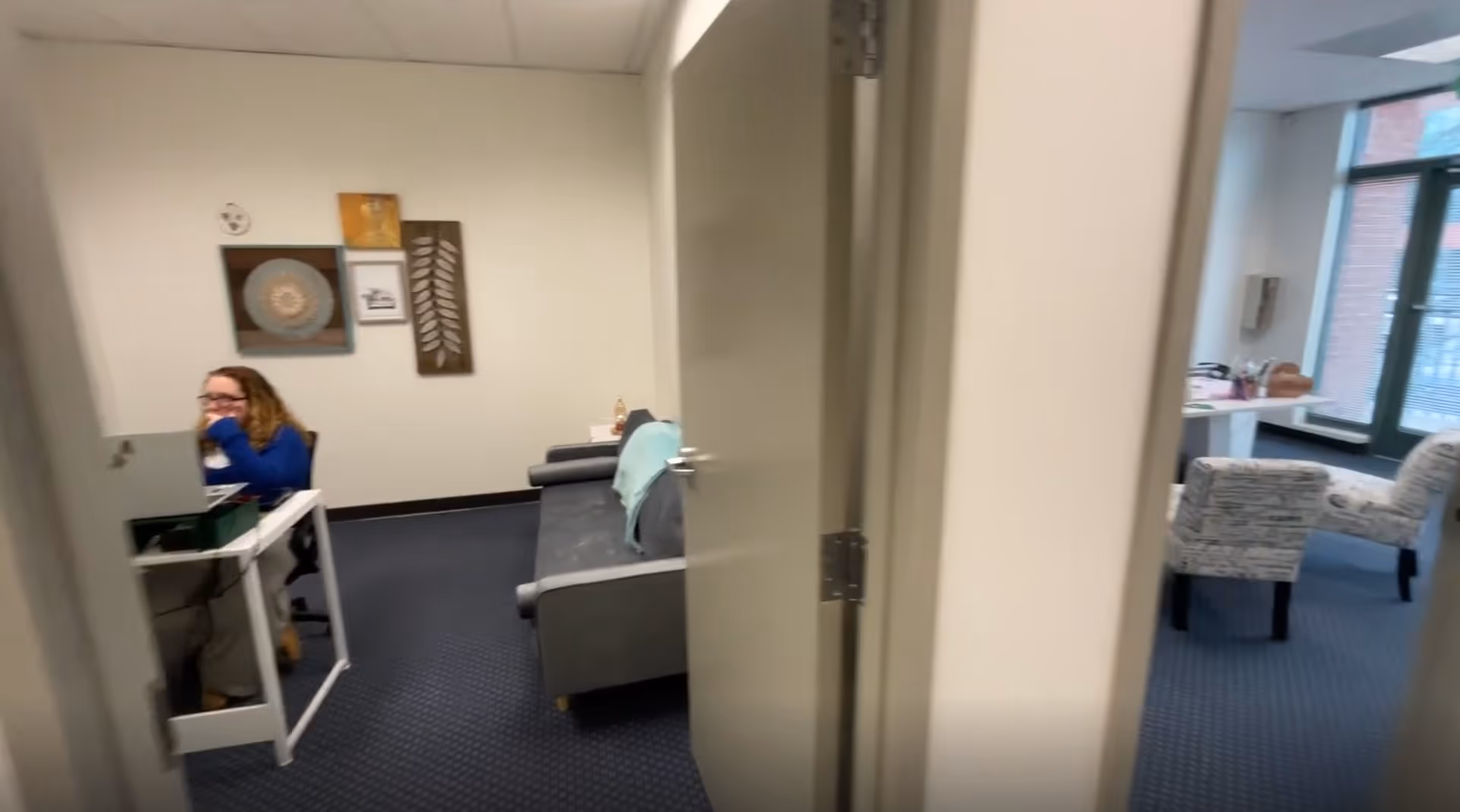 Office area and lounge inside a senior living facility, with a person at a desk.