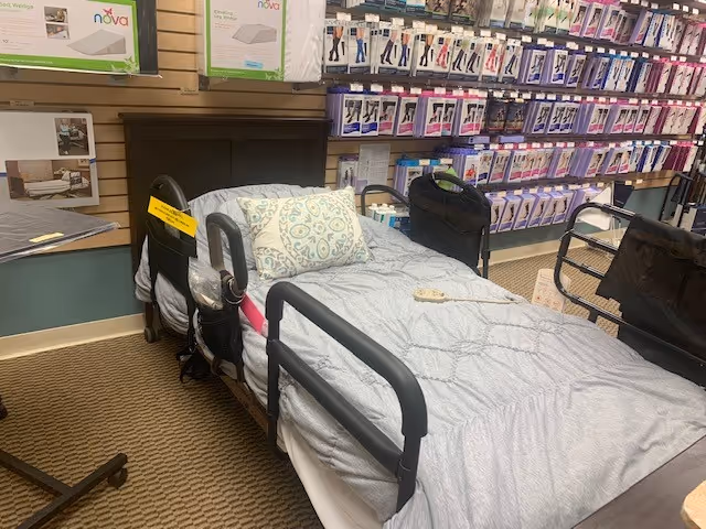 Hospital-style adjustable bed with side rails in a display area surrounded by boxed medical supplies.