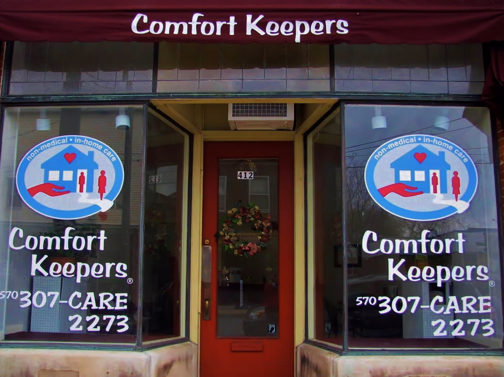 Storefront of Comfort Keepers Home Care with window decals and a red door