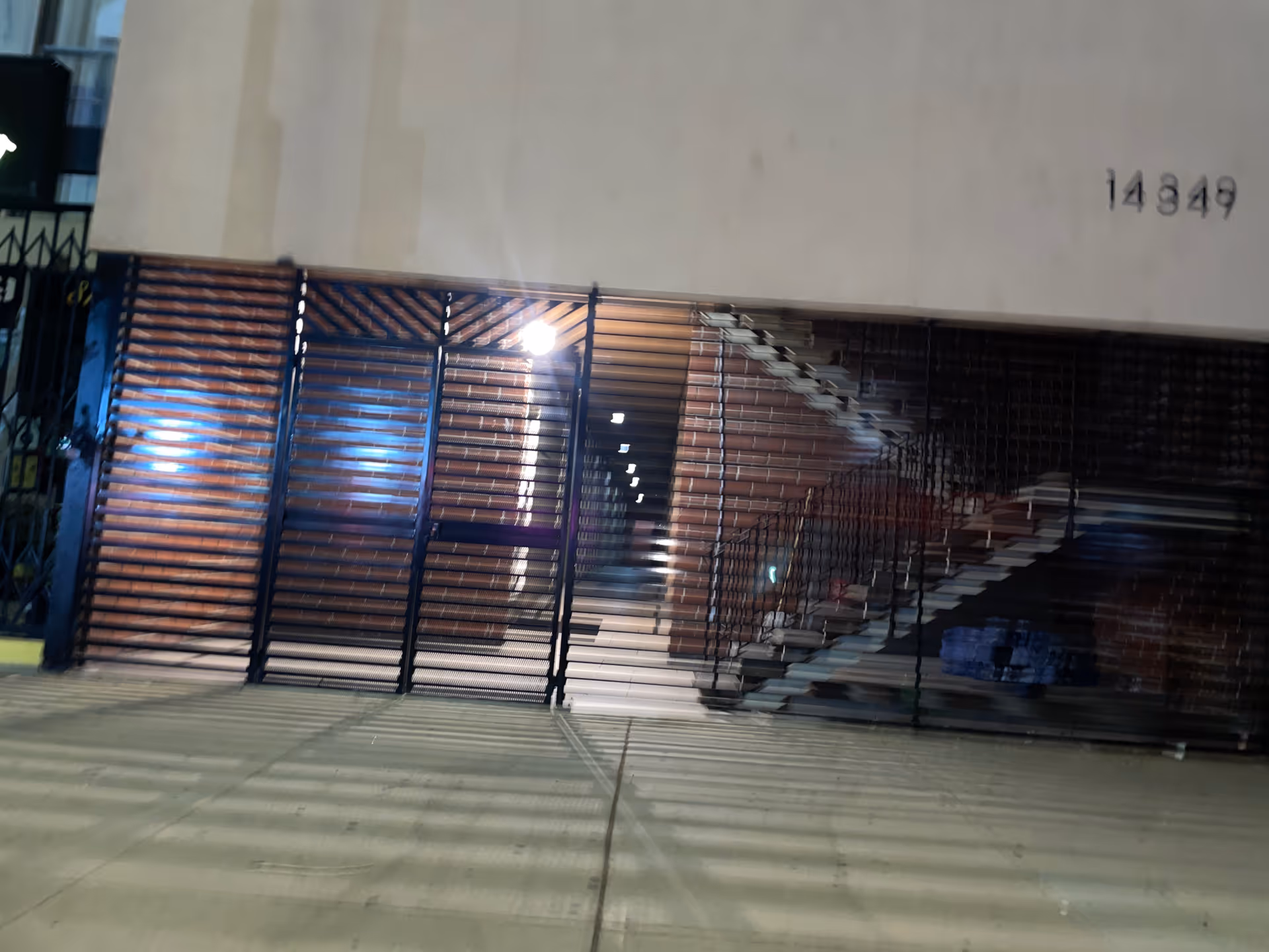 Exterior of a building with a metal slatted gate and visible interior stairs.