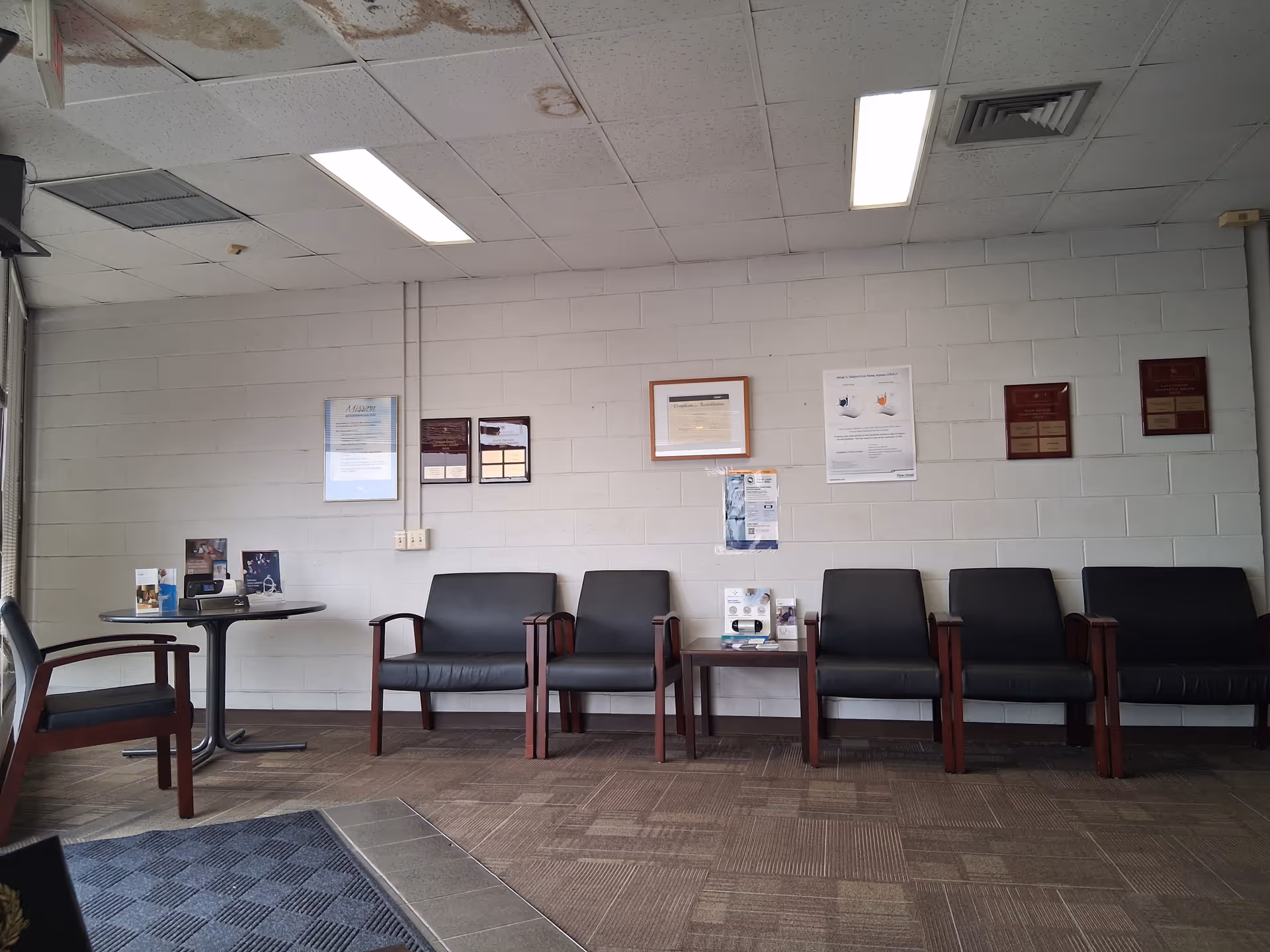 Row of black chairs against a light gray cinder-block wall in a waiting area.