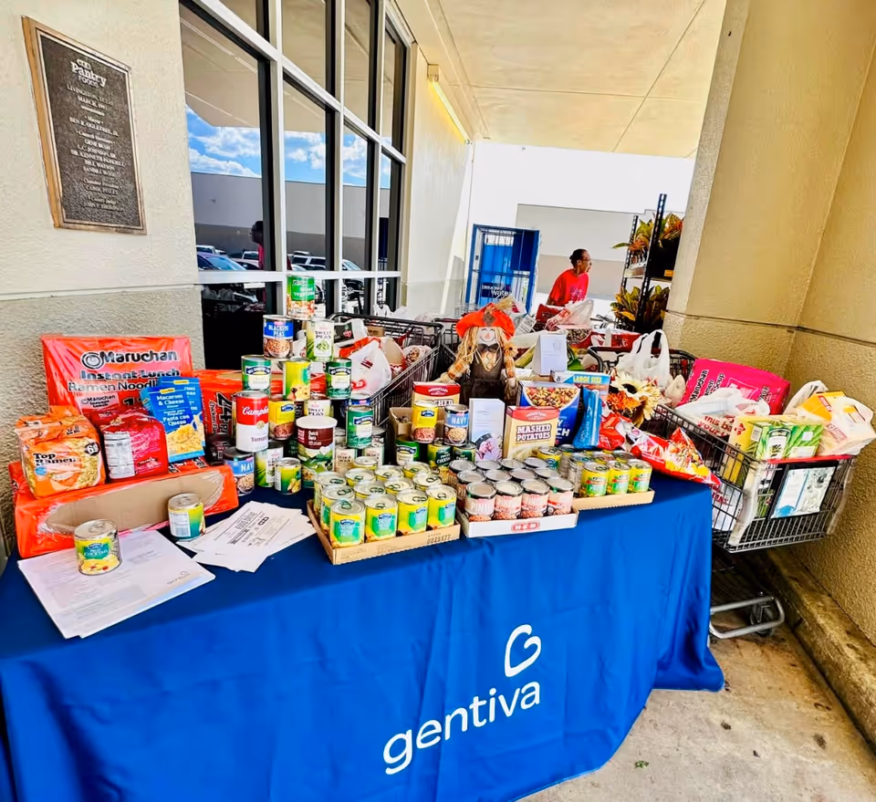 Table covered in blue Gentiva tablecloth displays canned goods and donated groceries outside.