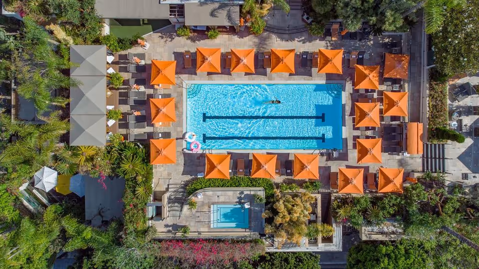 Aerial view of a resort-style outdoor pool with orange umbrellas and lounge chairs