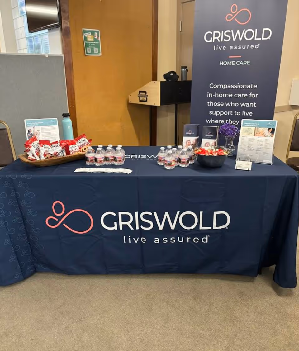 Promotional Griswold Home Care banner and table with water bottles and snacks indoors.