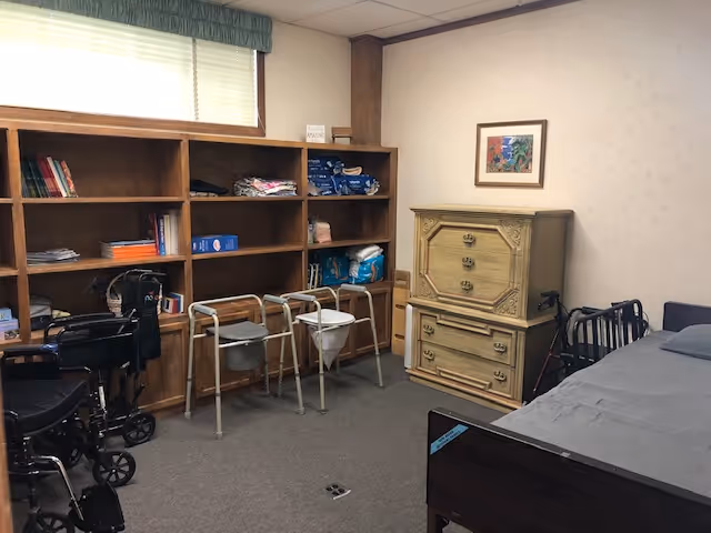 A bedroom with a bed, dresser, shelves, and walkers along the wall.