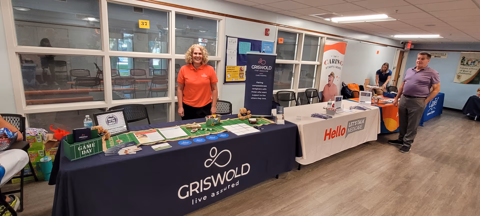 Visitors stand near vendor tables with banners inside a Griswold senior living facility hall.