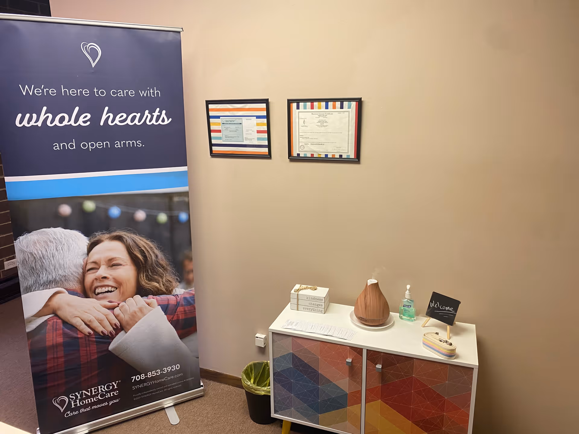 Interior lobby area featuring a SYNERGY HomeCare banner beside a small reception cabinet.