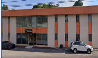Two-story orange and beige facility exterior with large windows and parked cars.