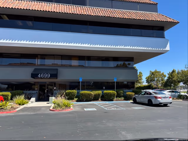 Exterior of a modern multi-story facility with a front entrance and surrounding parking.