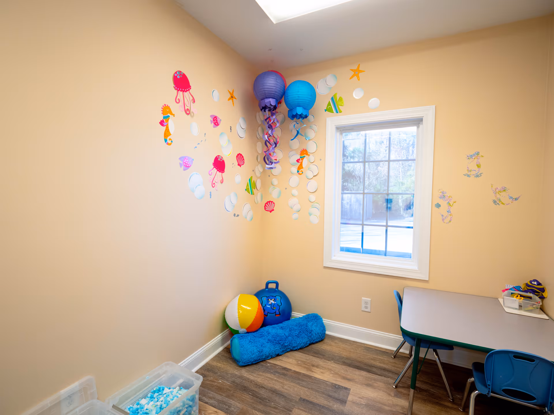 Colorful therapy room with wall decals, small table, chairs, and toys.