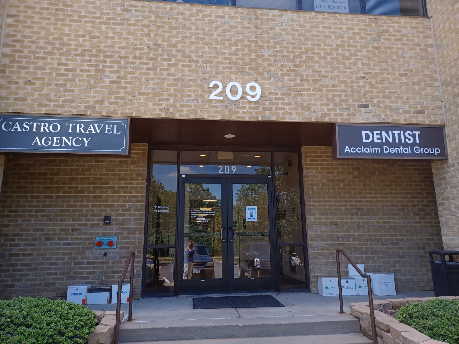Brick building entrance with large 209 and signs for a travel agency and dentist.