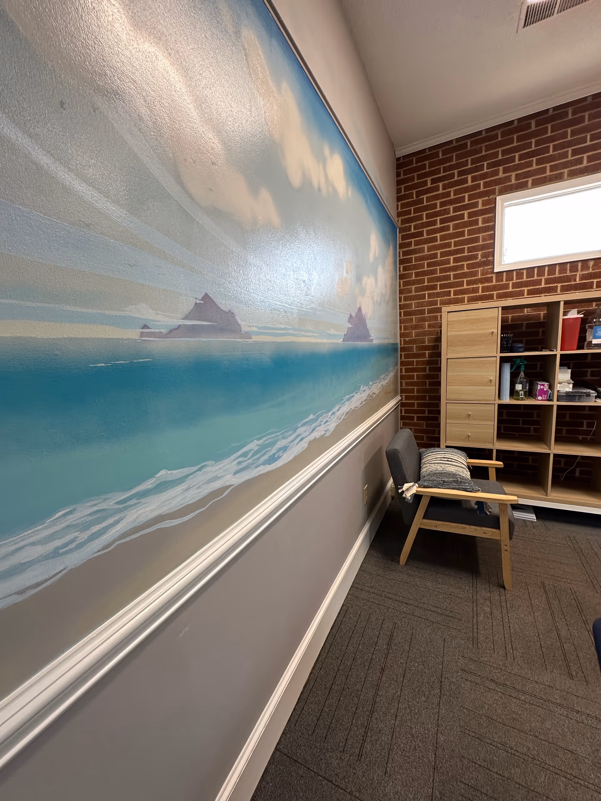 Interior hallway featuring a large ocean mural, brick wall, and wooden chair beside storage shelves.