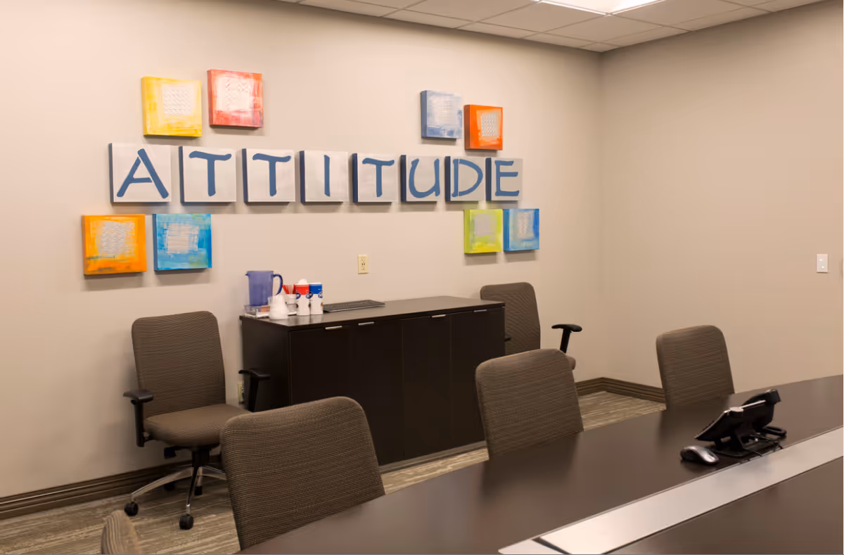 Conference room with wall art spelling 'ATTITUDE', a long table, and office chairs.