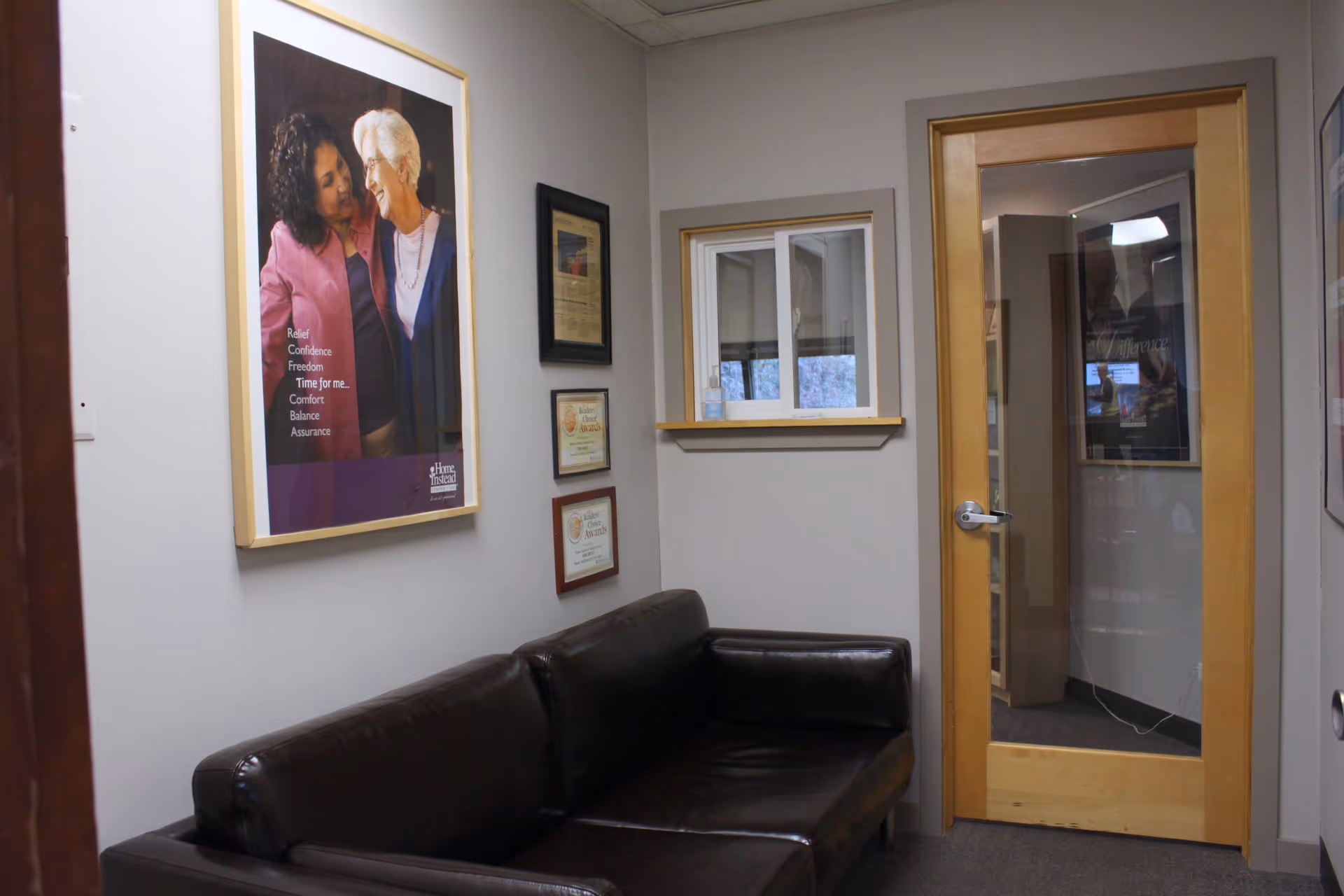 A waiting area with a black leather sofa, framed posters, and a wooden doorway.
