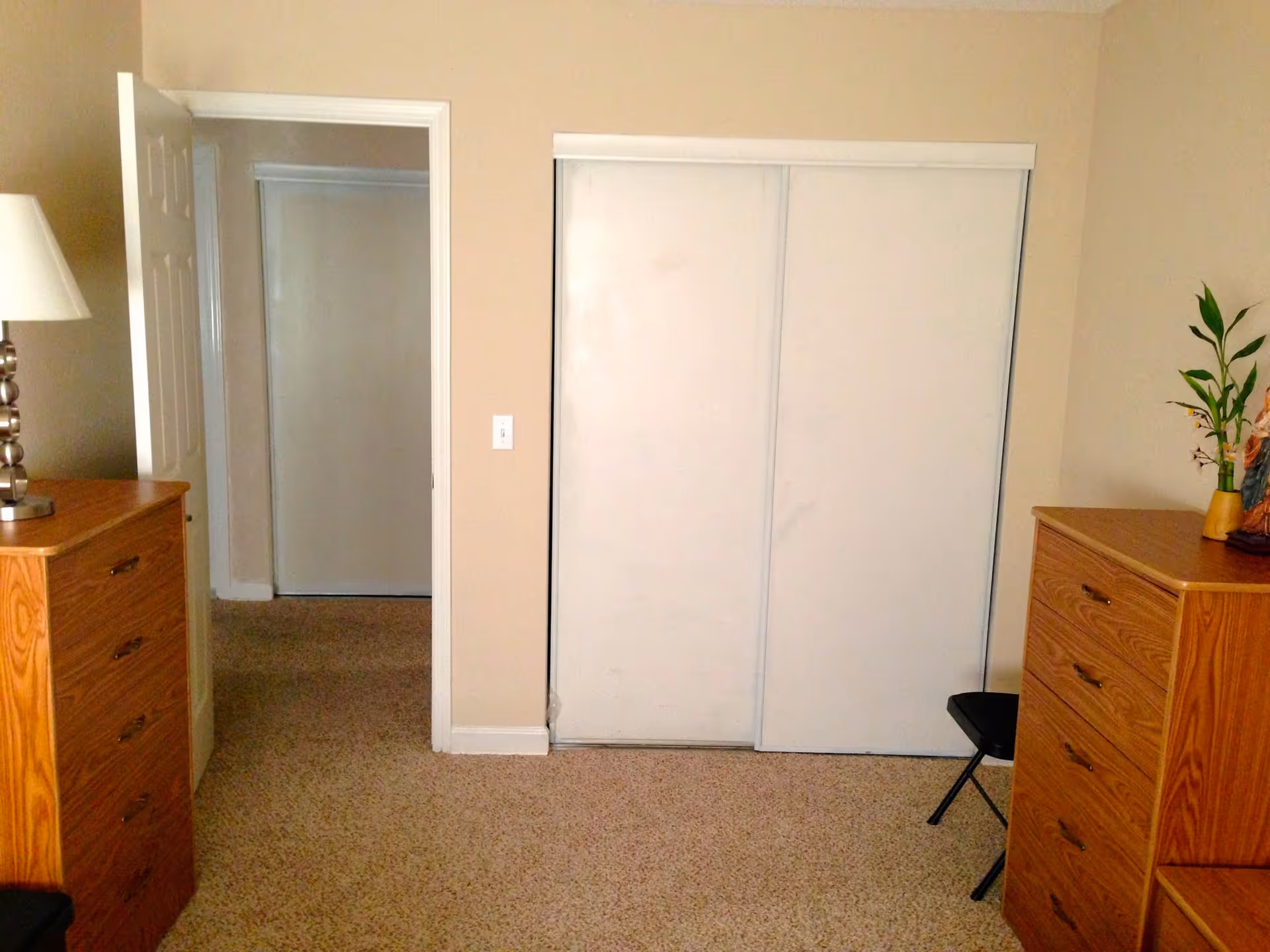 Neat bedroom with two wooden dressers, a lamp, and a closed white closet.