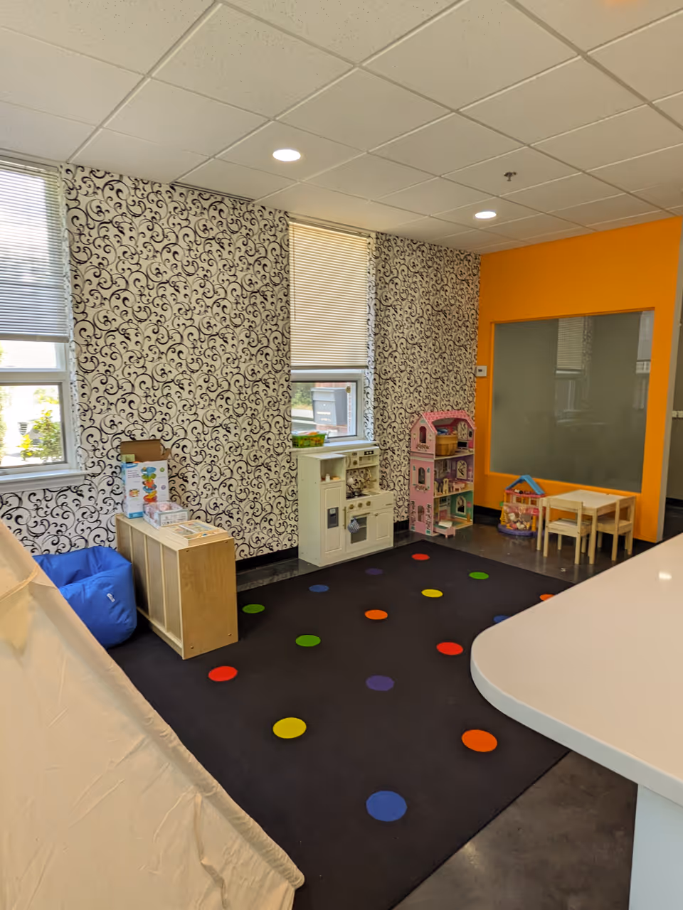 Indoor playroom with patterned wallpaper, colorful floor dots, and toy furniture.