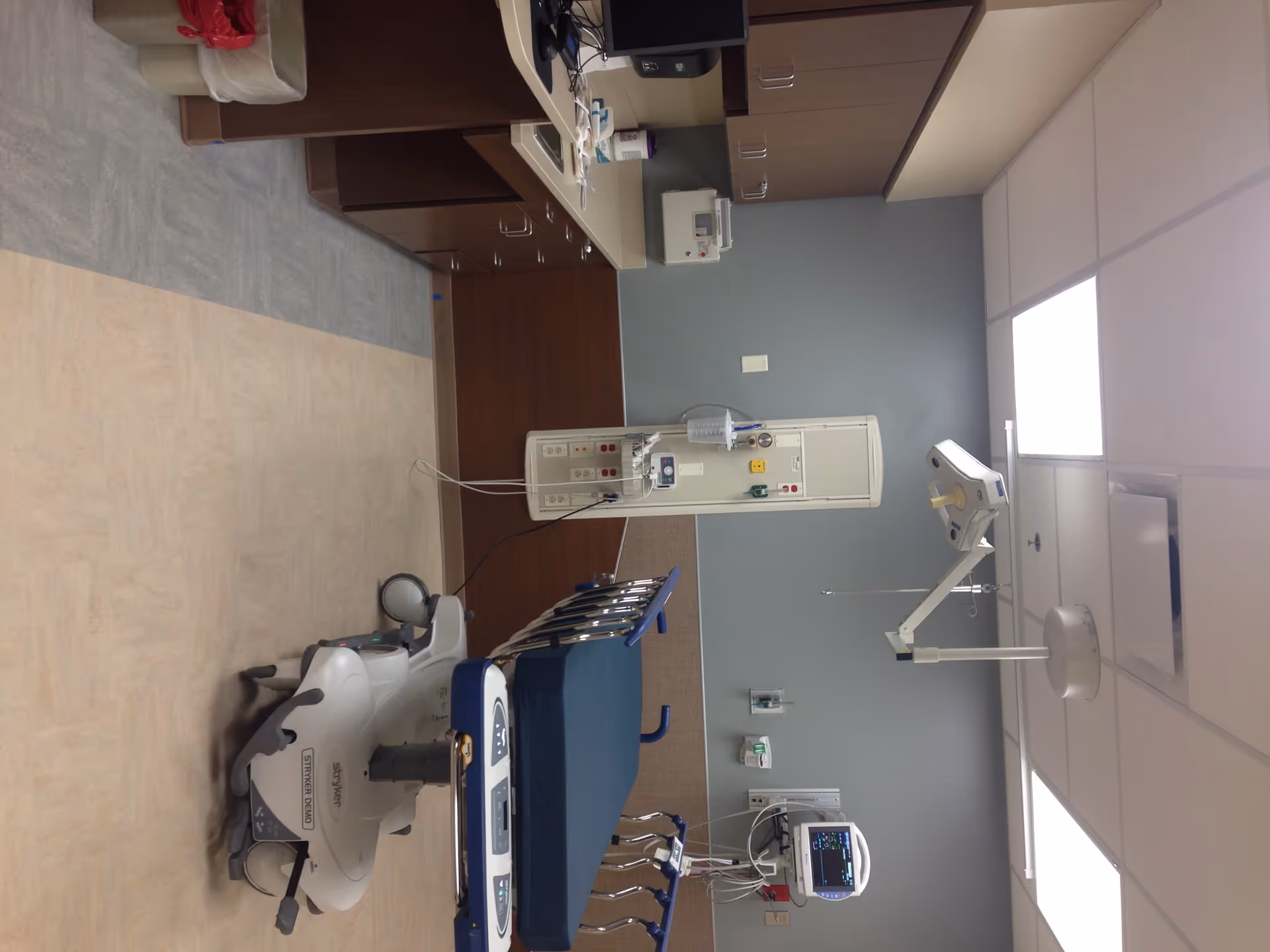 Hospital patient room with medical equipment, beds, monitors, and overhead lighting.