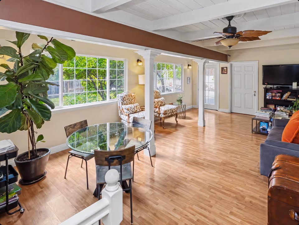 Bright senior living room with round glass dining table, seating, and plants.