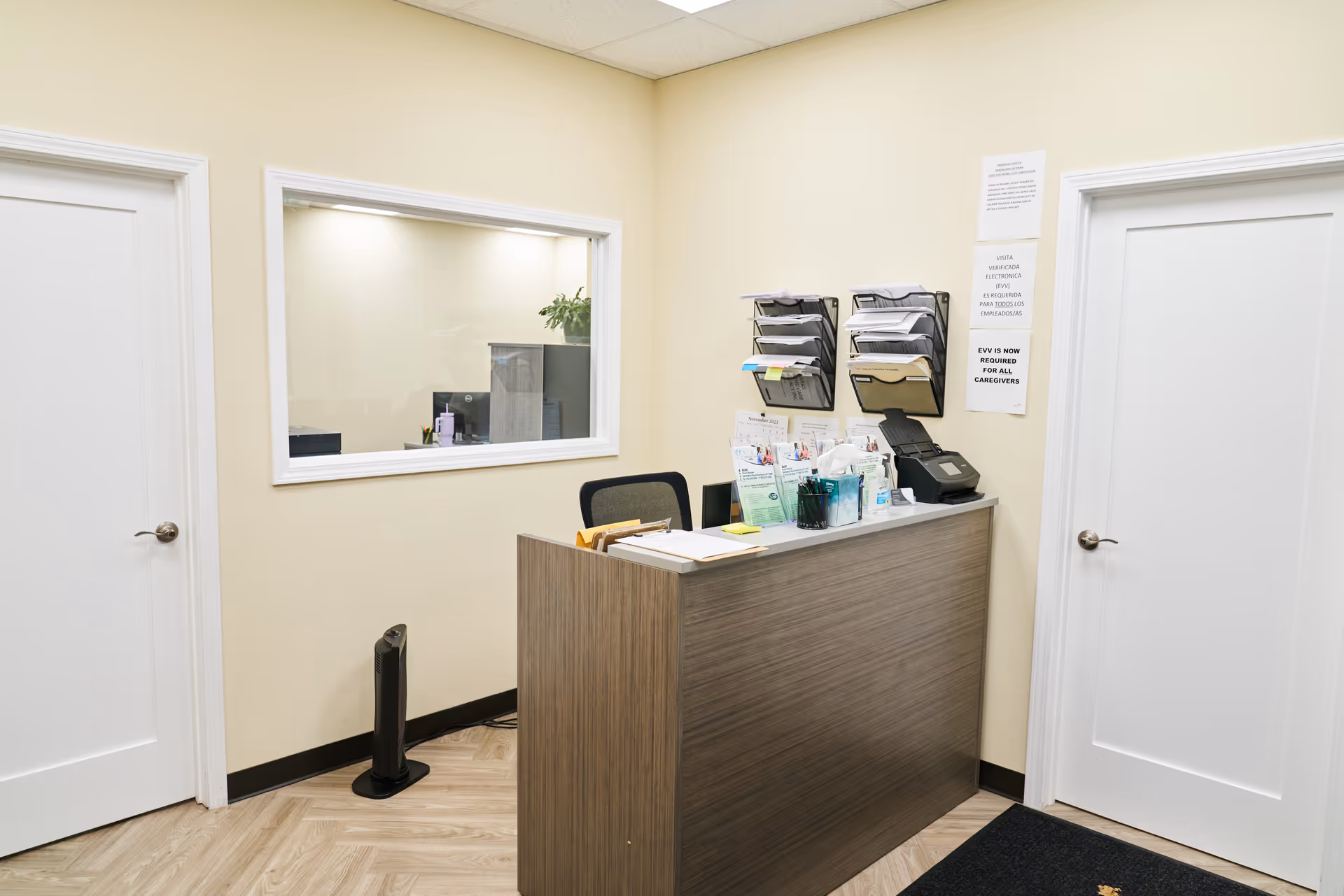 Reception desk with brochures and a window view in a beige hallway.