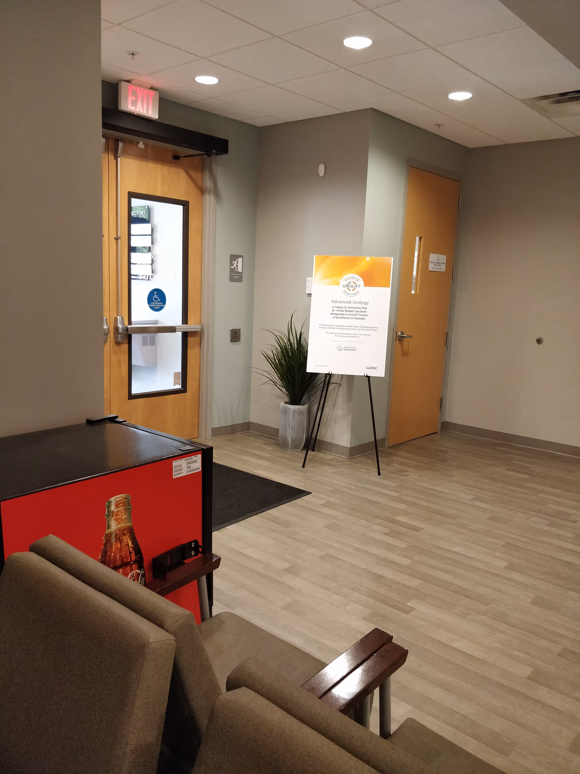 Interior lobby area with seating, a doorway, signboard, and a potted plant.