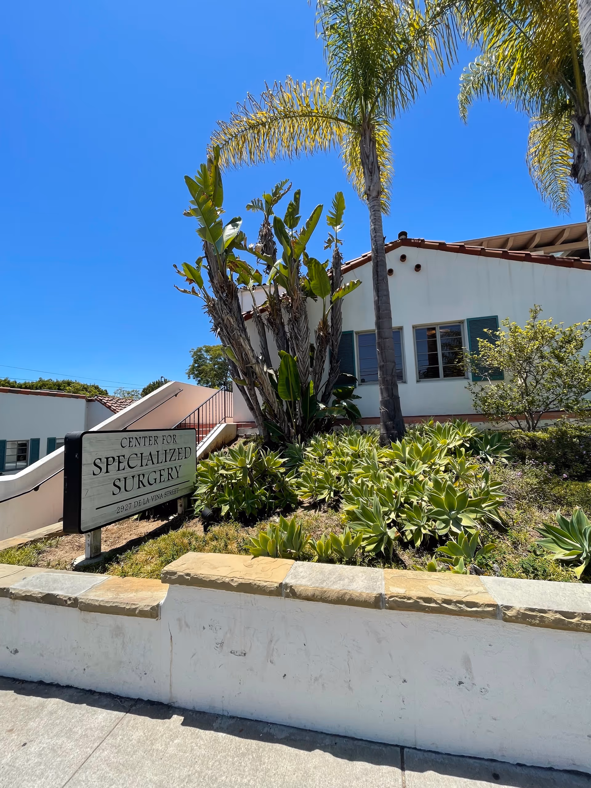 Exterior view of a white building with 'Center for Specialized Surgery' sign and tropical plants.