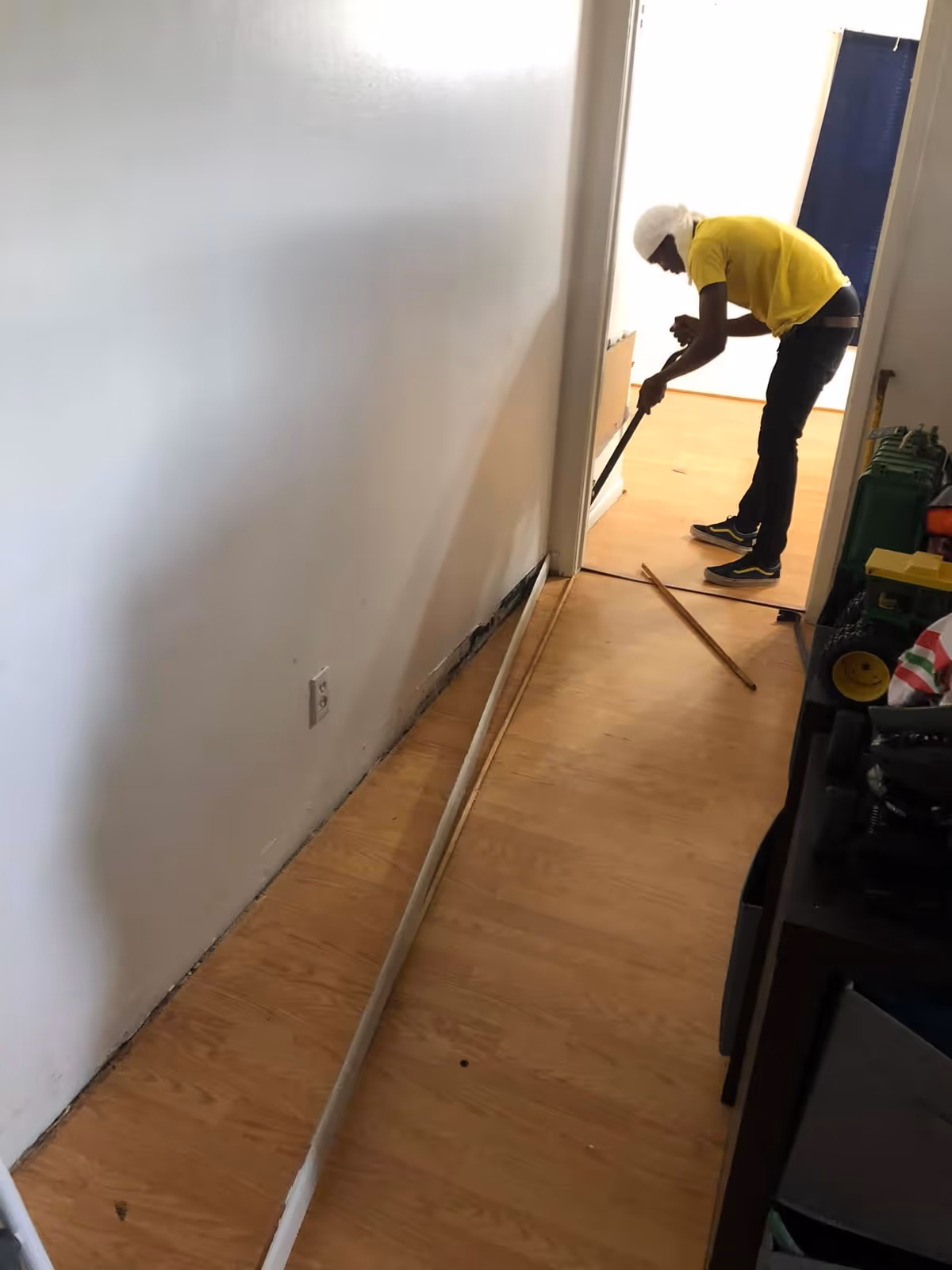 Maintenance worker in yellow shirt and white hard hat repairing hallway interior.