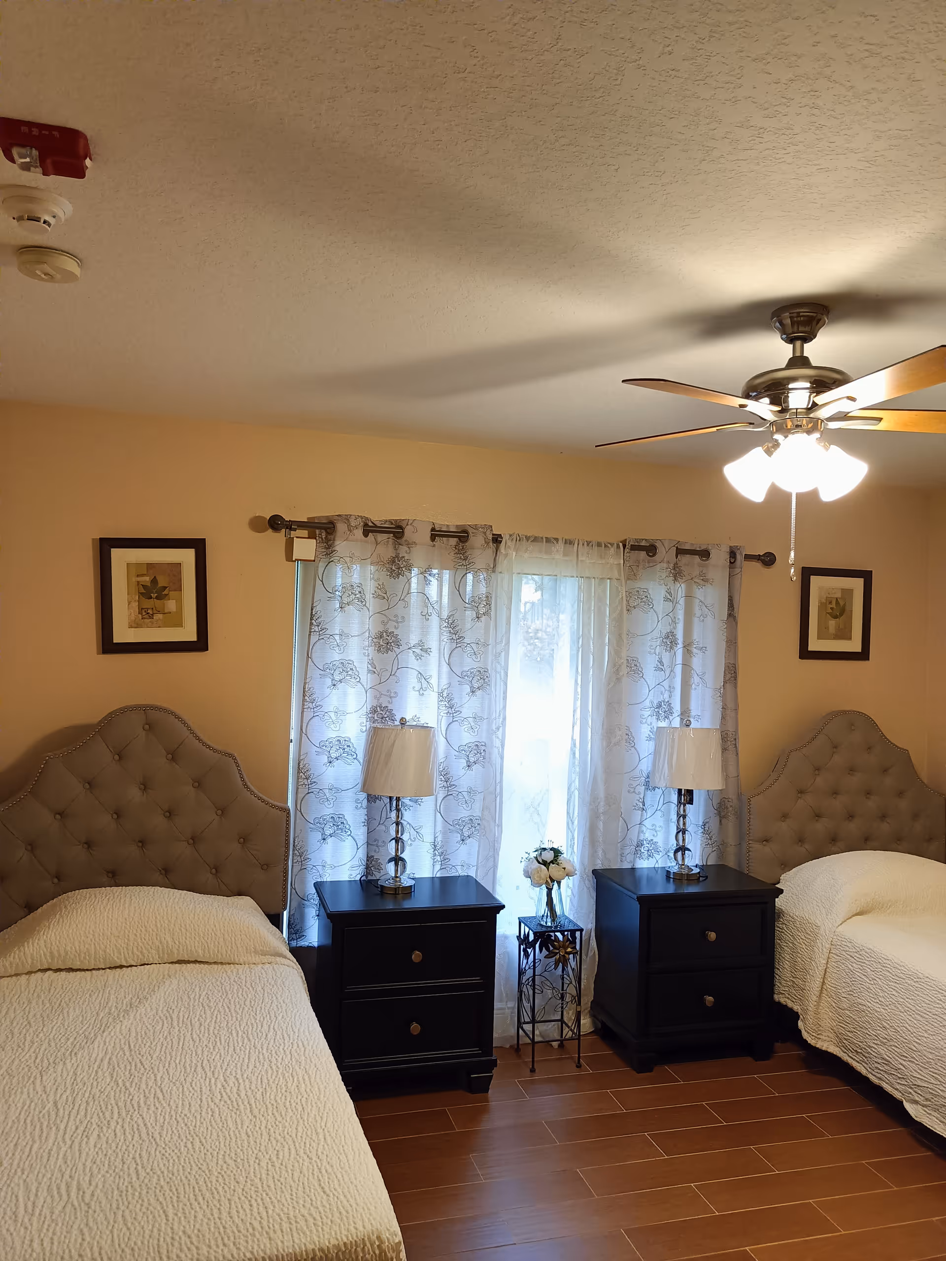 Two twin beds with tufted headboards, matching nightstands, lamps, and sheer curtains.